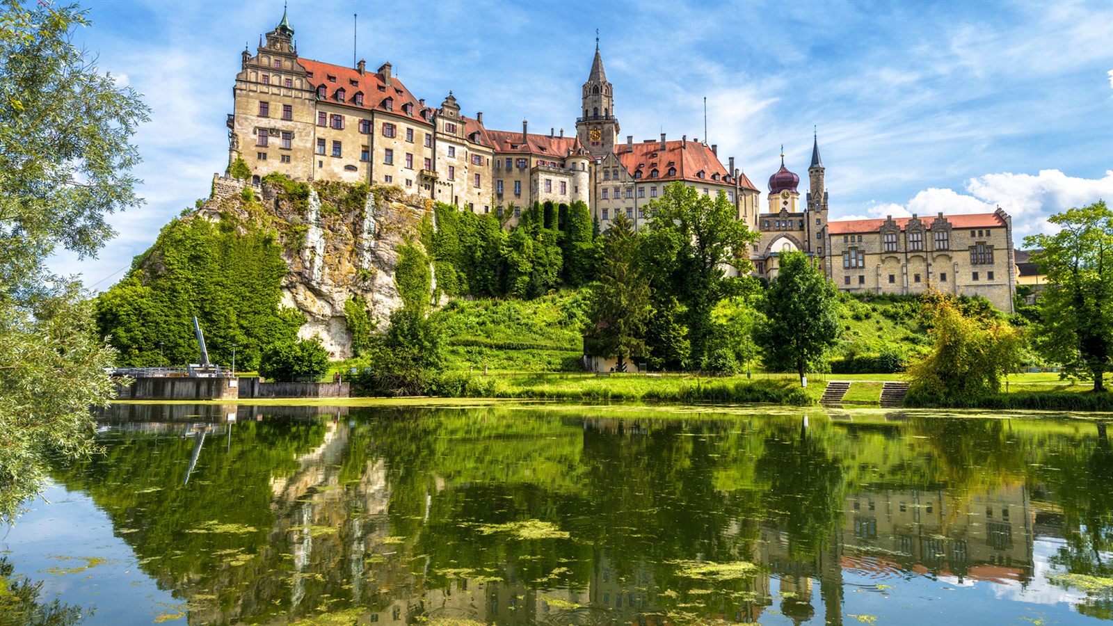 Hilltop castle above a calm river, reflected in the water on a sunny day