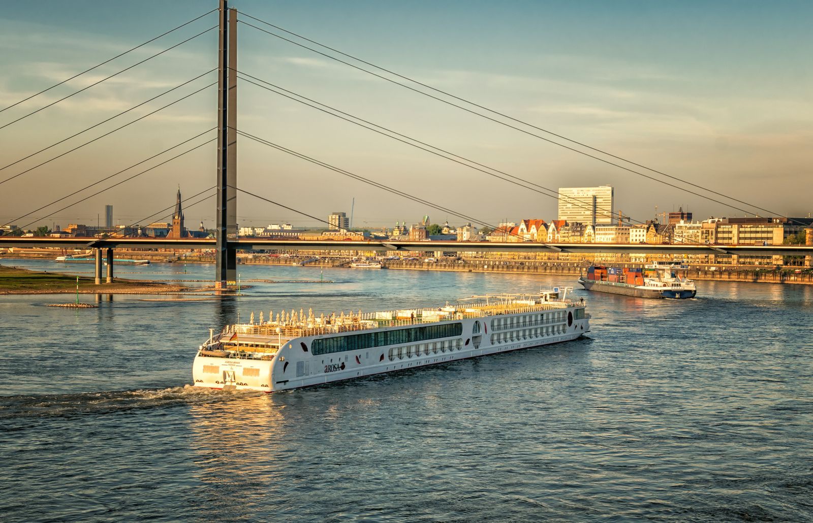 River cruise ship sailing under a cable-stayed bridge at golden hour, the kind of scene a first time river cruise brings